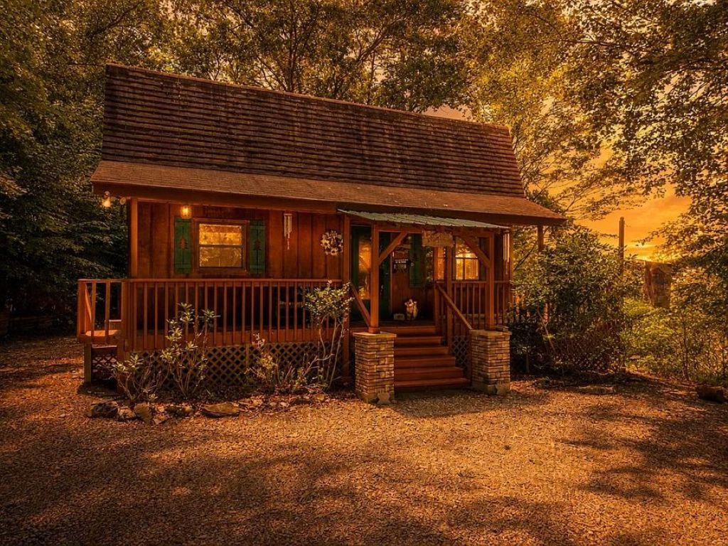 A wooden cabin with a porch, surrounded by trees.