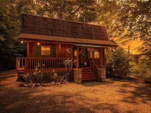 A wooden cabin with a porch, surrounded by trees.
