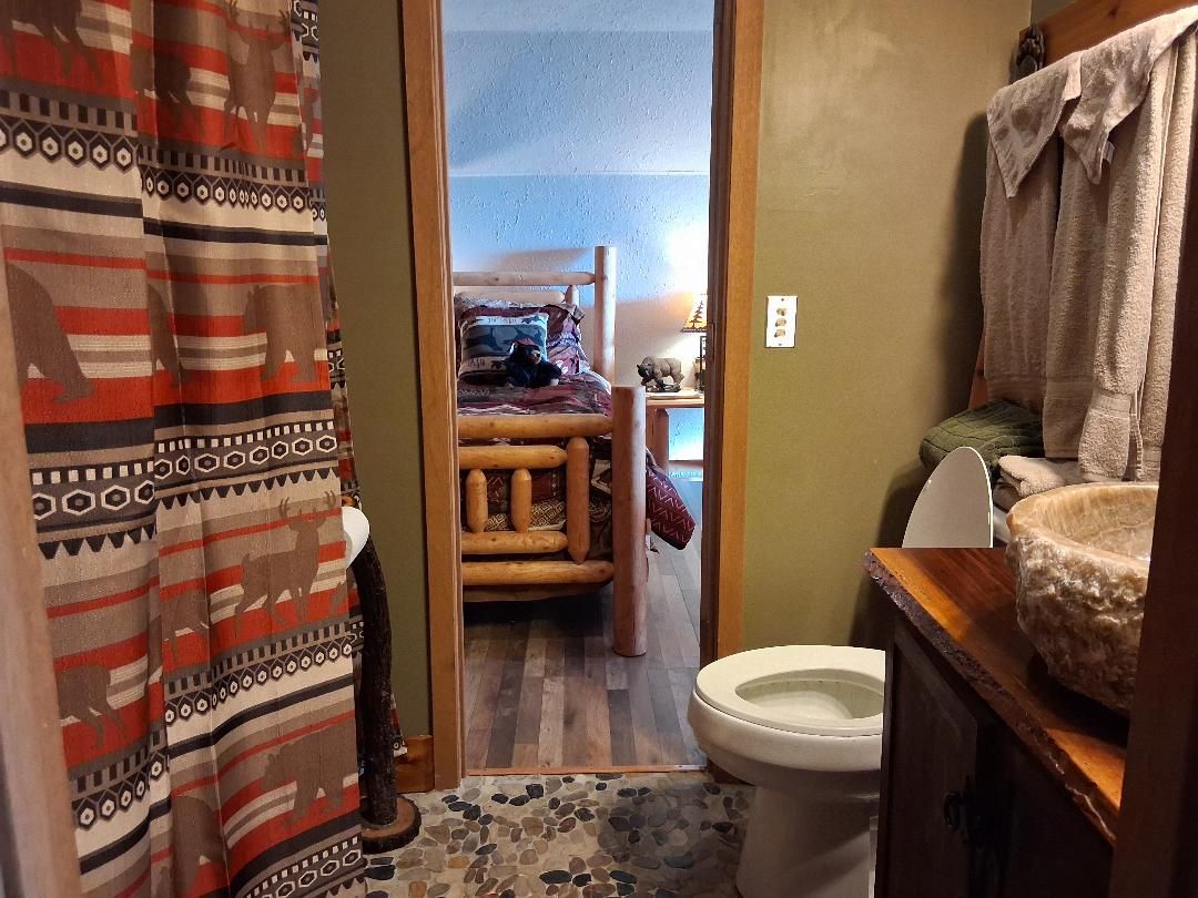 A bathroom with a rustic wooden bed, a stone-tiled floor, a white toilet, and a wooden vanity with a stone basin.