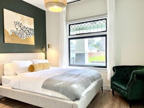 A bedroom with a bed, a green armchair, a window with a view, and a wall-mounted artwork. - New Modern Craftsman Guest House with Bay Windows (San Jose)