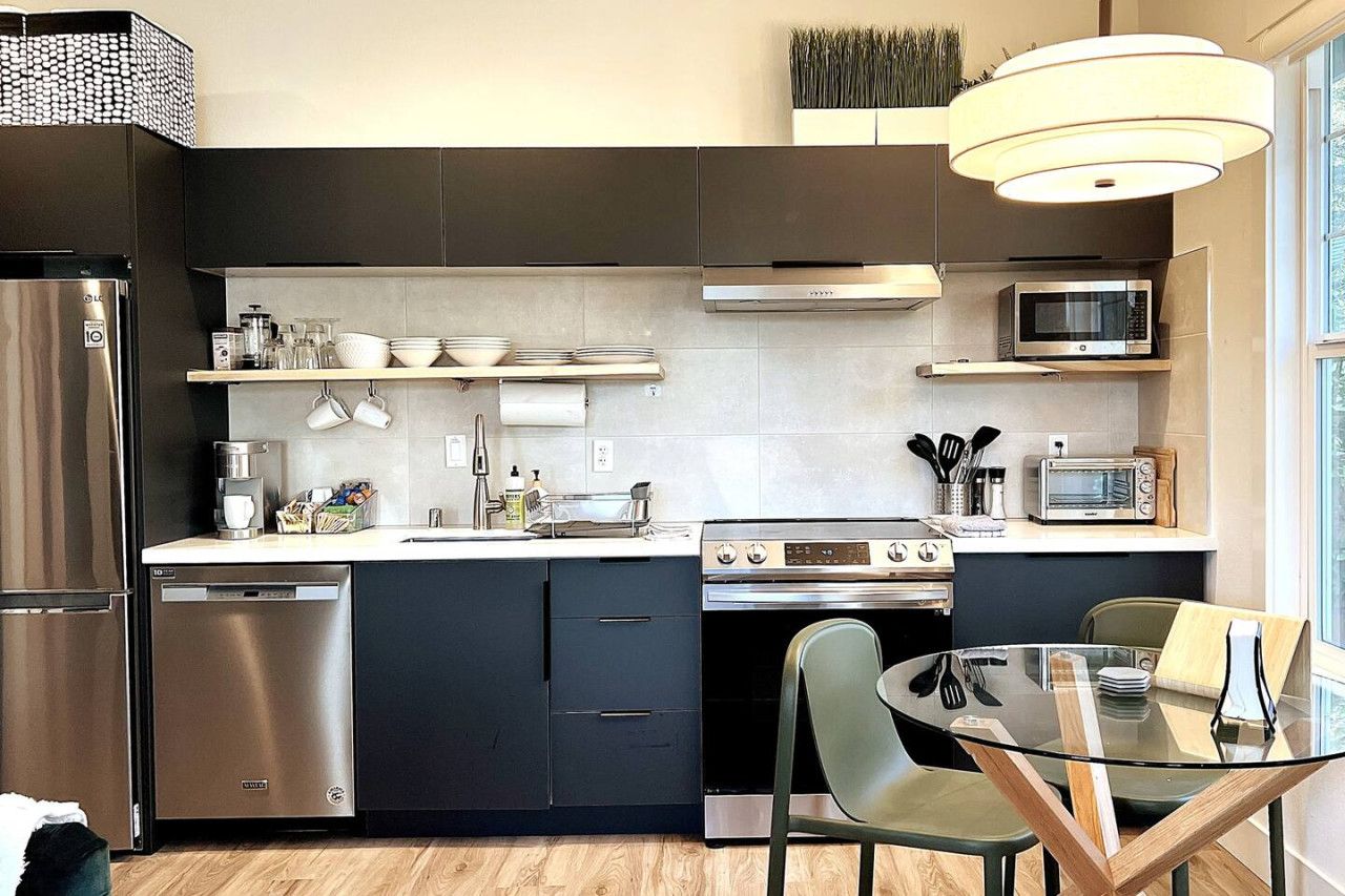 A modern kitchen with a built-in dishwasher, a microwave, and a stove. There is a dining table with chairs and a hanging light fixture above.