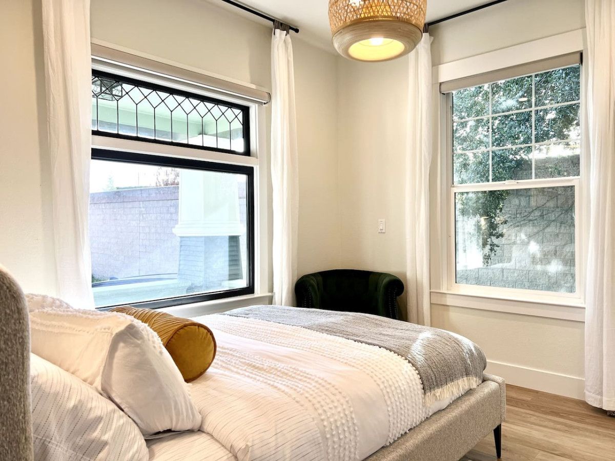 Una camera da letto con un letto, due finestre, una sedia e un lampadario.