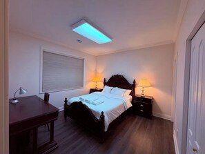 Ein Schlafzimmer mit Bett, Nachttischen, einem Schreibtisch und einer Deckenleuchte.