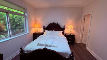 A neatly made bed with white linens and two bedside tables with lamps, a skylight above, and a view of greenery through the window.