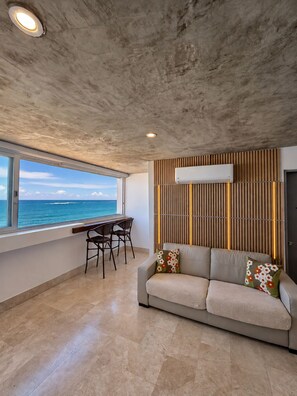 A modern living room with a view of the ocean, a sofa with floral cushions, and a dining area with chairs. - Gorgeous Condado 3-Bedroom + 2 Bath w/ OceanView! (San Juan)