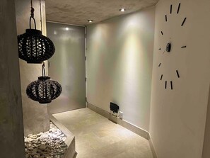Ein Flur mit einer Uhr an der Wand, einer Betonstütze und zwei hängenden Laternen.