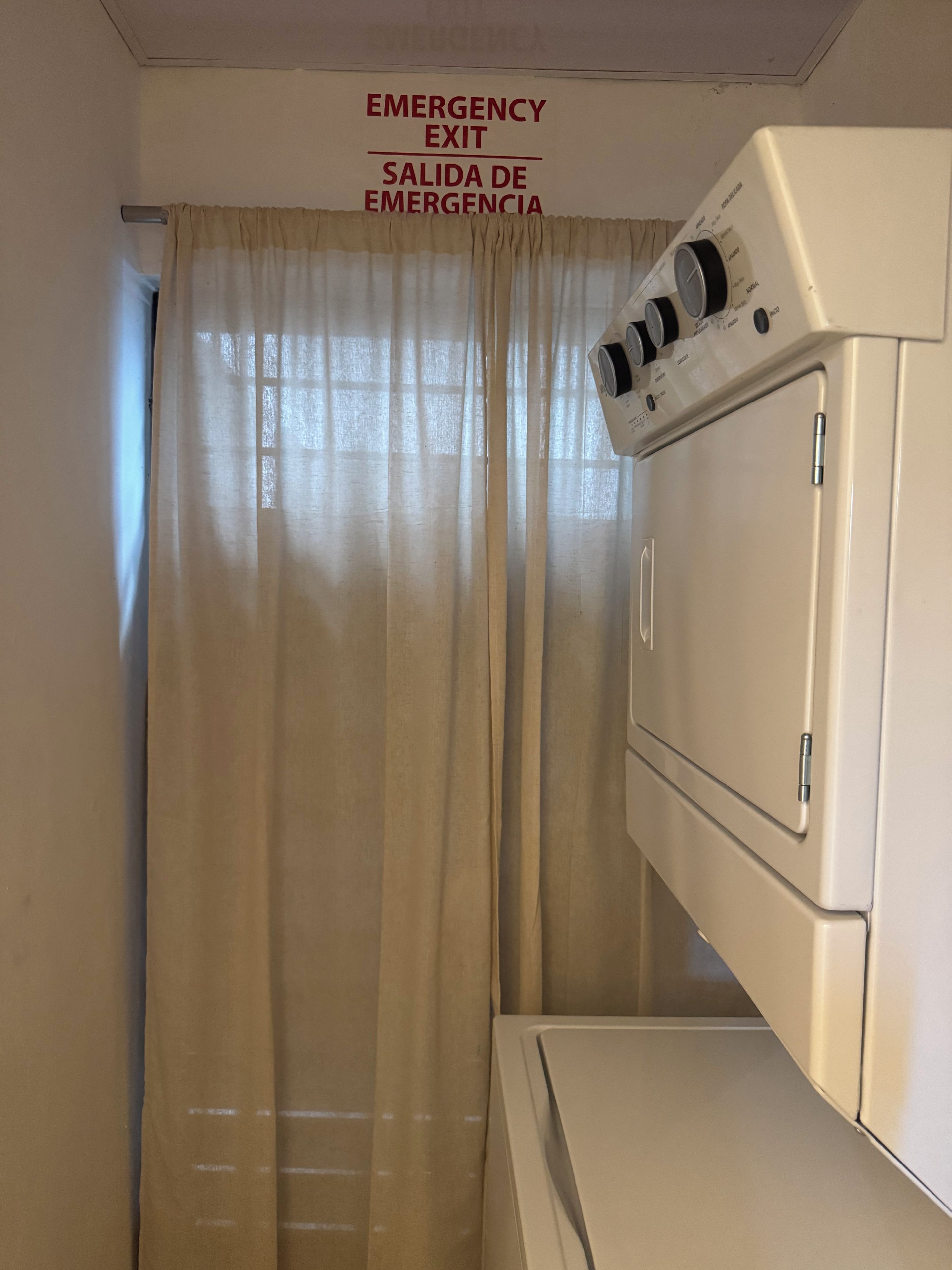 Lavandería con lavadora y un letrero que indica una salida de emergencia.