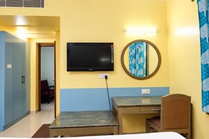 Habitación de hotel con cama, escritorio, silla, televisor, espejo y armario.