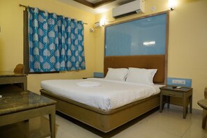 A hotel room with a bed, a bedside table, a nightstand, a desk, and a window with curtains. - MIMO Hotels (Walajapet)