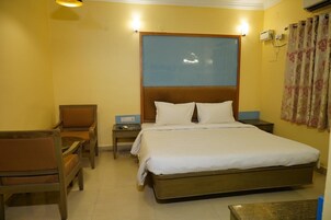 Ein Hotelzimmer mit Bett, Sessel, Nachttisch und Wand-Klimaanlage.