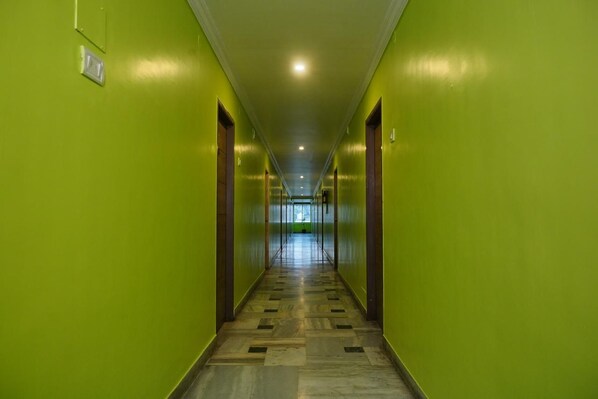 Un pasillo con paredes verdes y piso estampado, que conduce a una habitación luminosa al final.