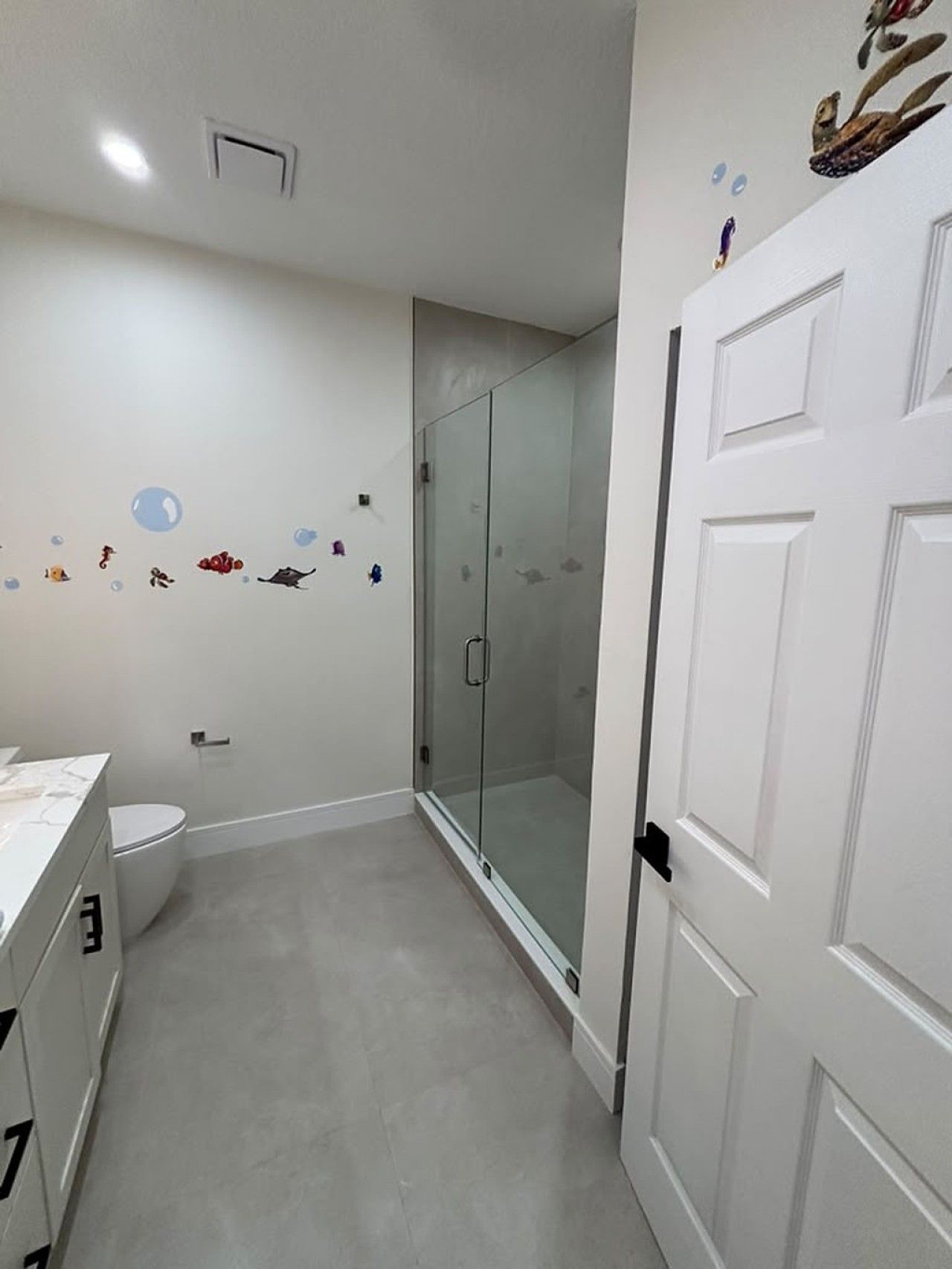 A bathroom with a toilet, a shower with glass doors, and a white door.