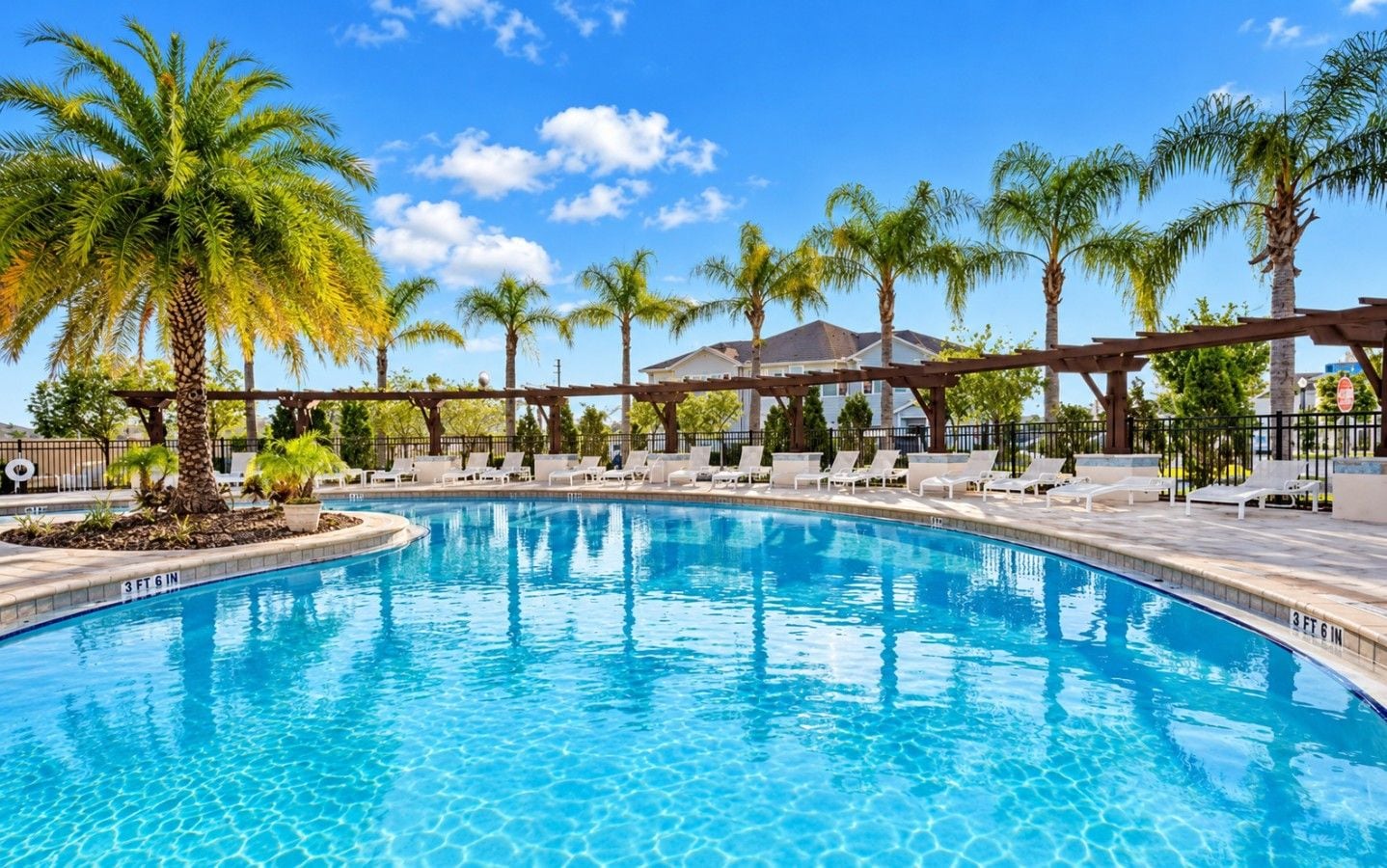 A swimming pool with lounge chairs, palm trees, and a clear blue sky.