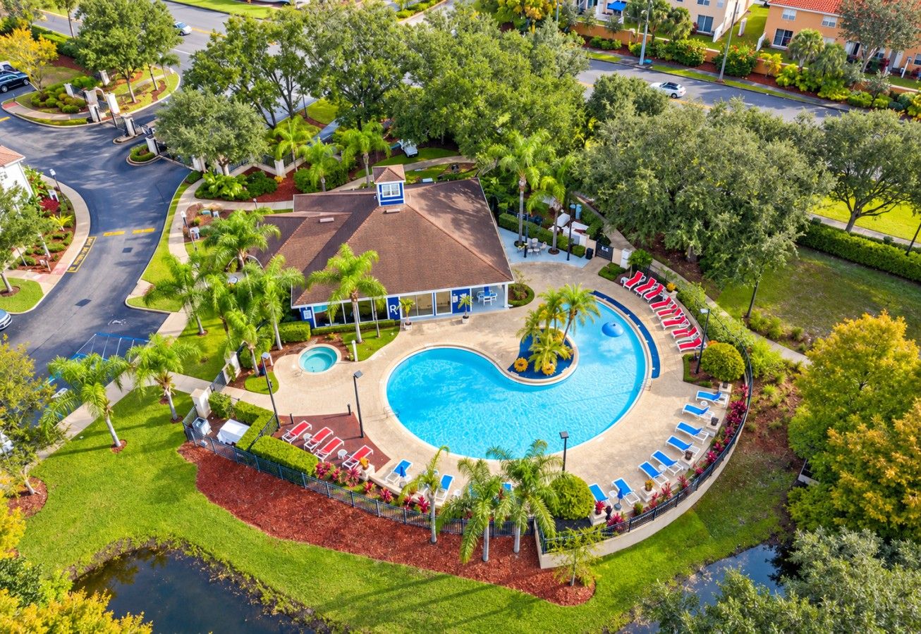A resort with a large swimming pool, a covered area with seating, and a building with a red roof.