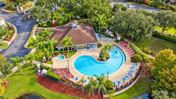 A resort with a large swimming pool, a covered area with seating, and a building with a red roof.