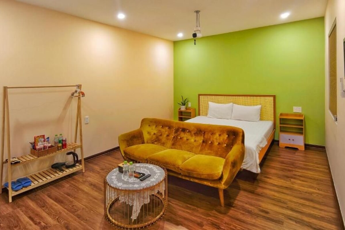 Una habitación con cama, sofá, una mesita redonda, estante con artículos de aseo personal e iluminación colgante.