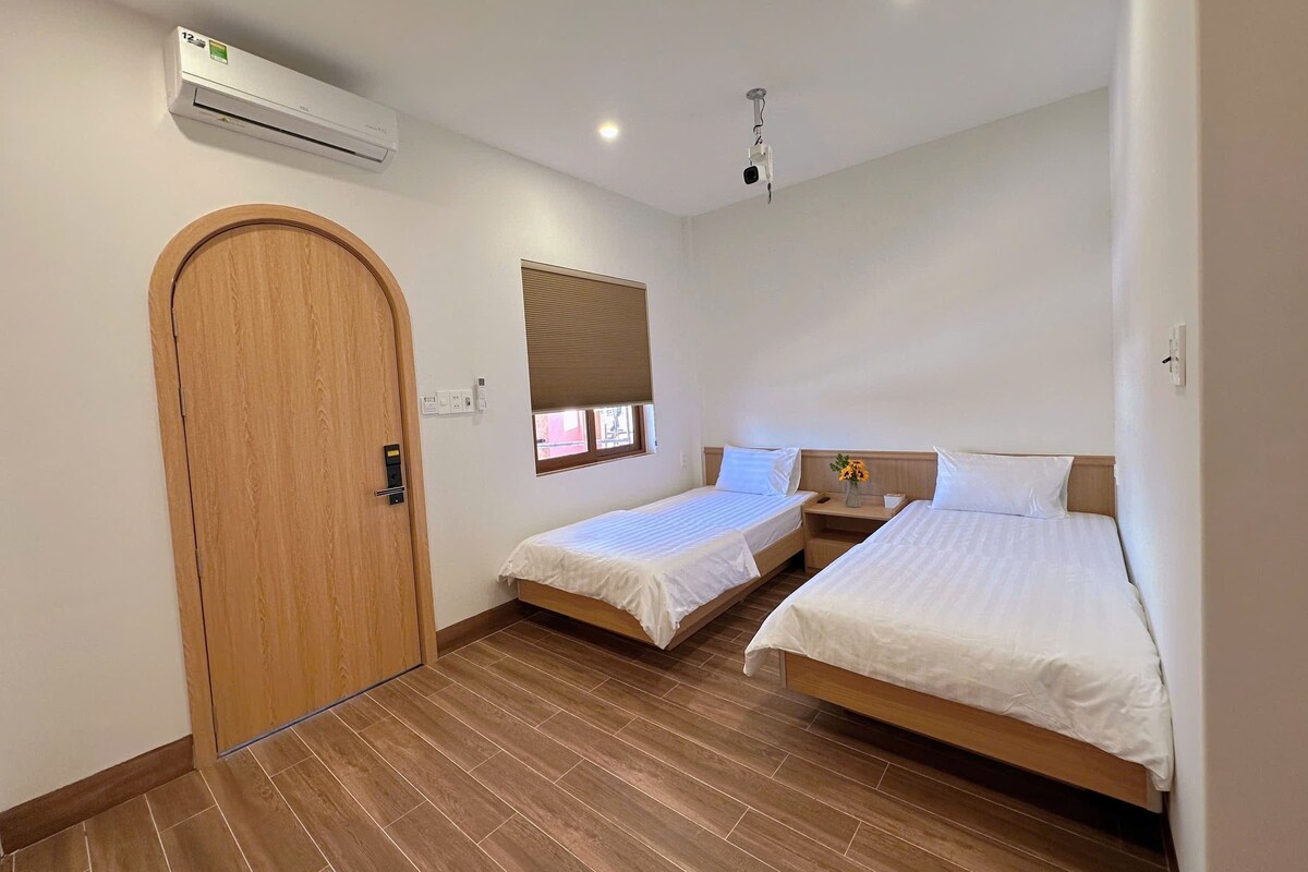 Una habitación con dos camas, una puerta de madera, un equipo de aire acondicionado, una lámpara en el techo y una ventana con persianas.