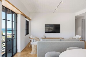 A modern living room with a large window, a flat-screen TV, and a grey sofa. - Architect-Designed 3-Bed by Bondi Beach (Bondi Beach)