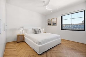 Ein Schlafzimmer mit einem großen Bett, einem Nachttisch, einem Deckenventilator und einem Fenster mit Solaranlagen.
