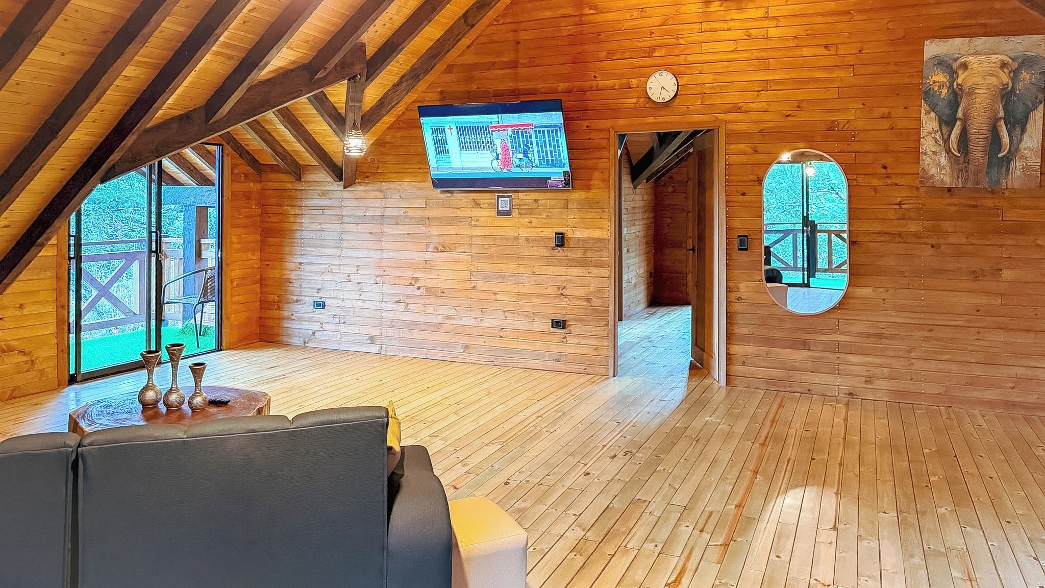 A cozy wooden cabin with a television mounted on the wall, a clock, and a door leading outside.