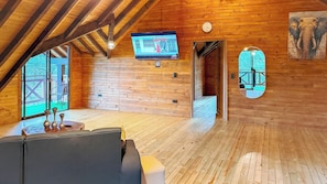 Uma cabana de madeira acolhedora, com televisão na parede, um relógio e uma porta para o exterior.
