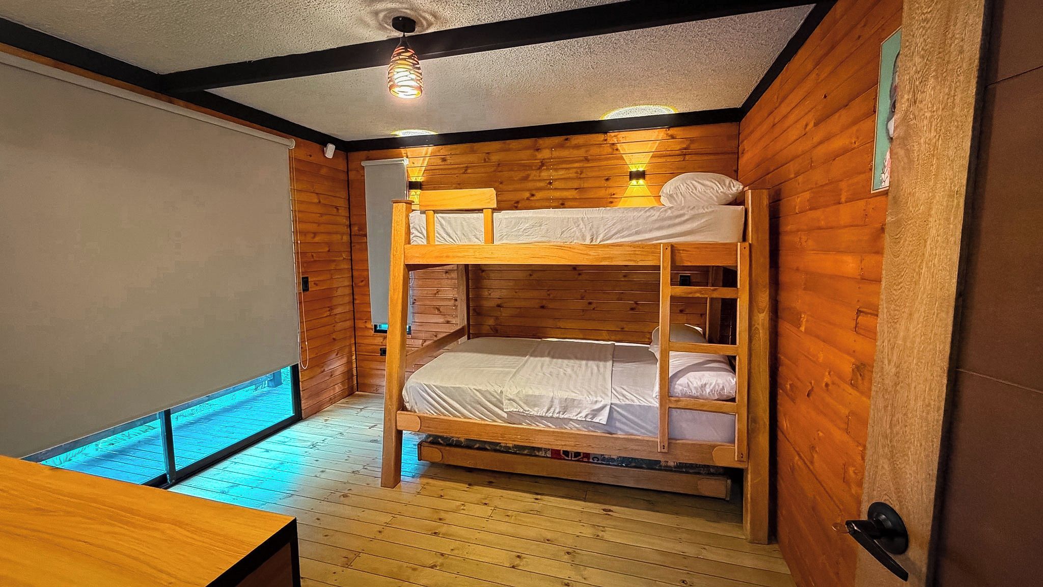 Habitación con literas, paredes de madera, una lámpara en el techo y suelo de madera.