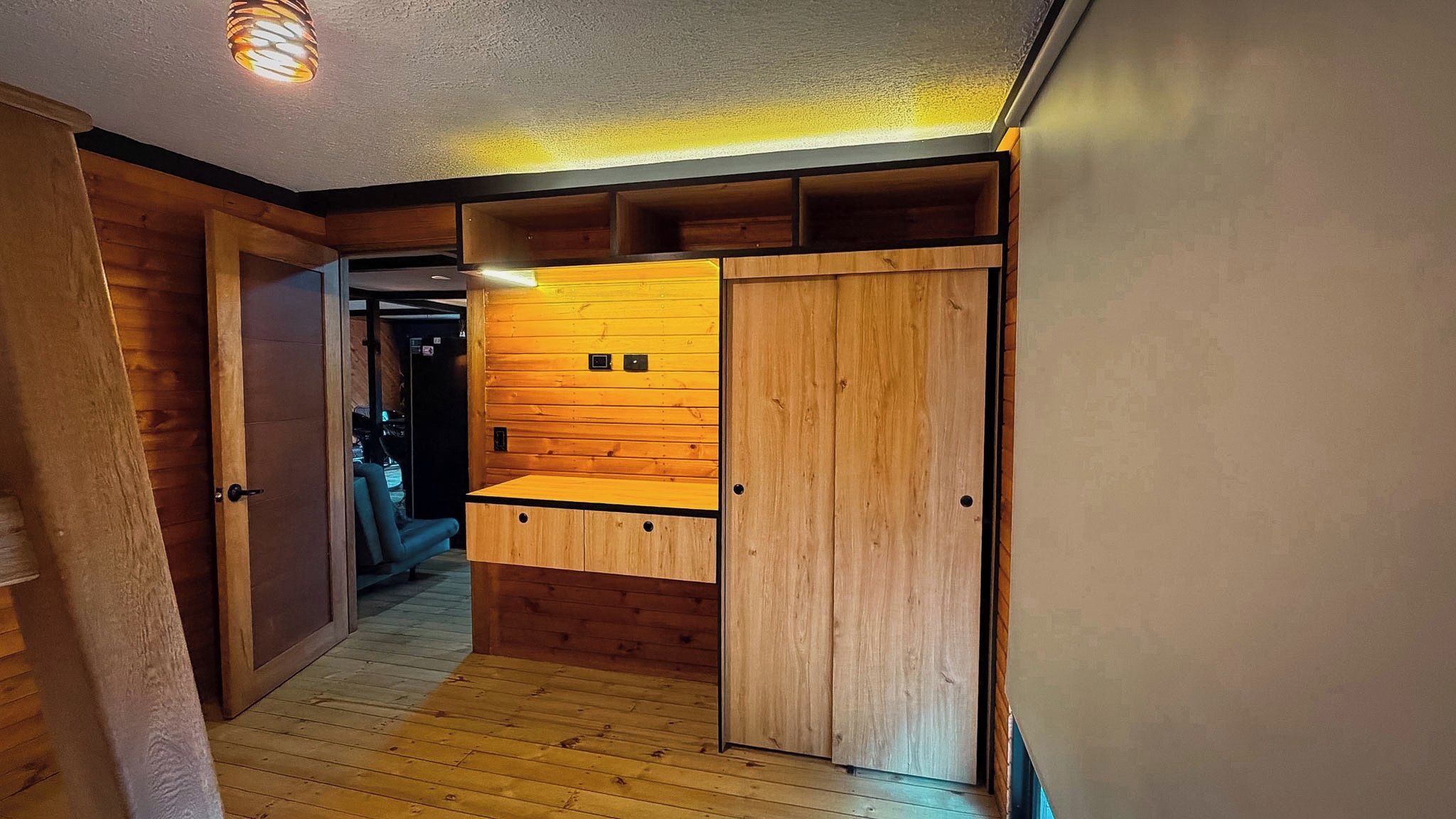 A hallway with wooden flooring, a built-in bench, and a door leading to another room.