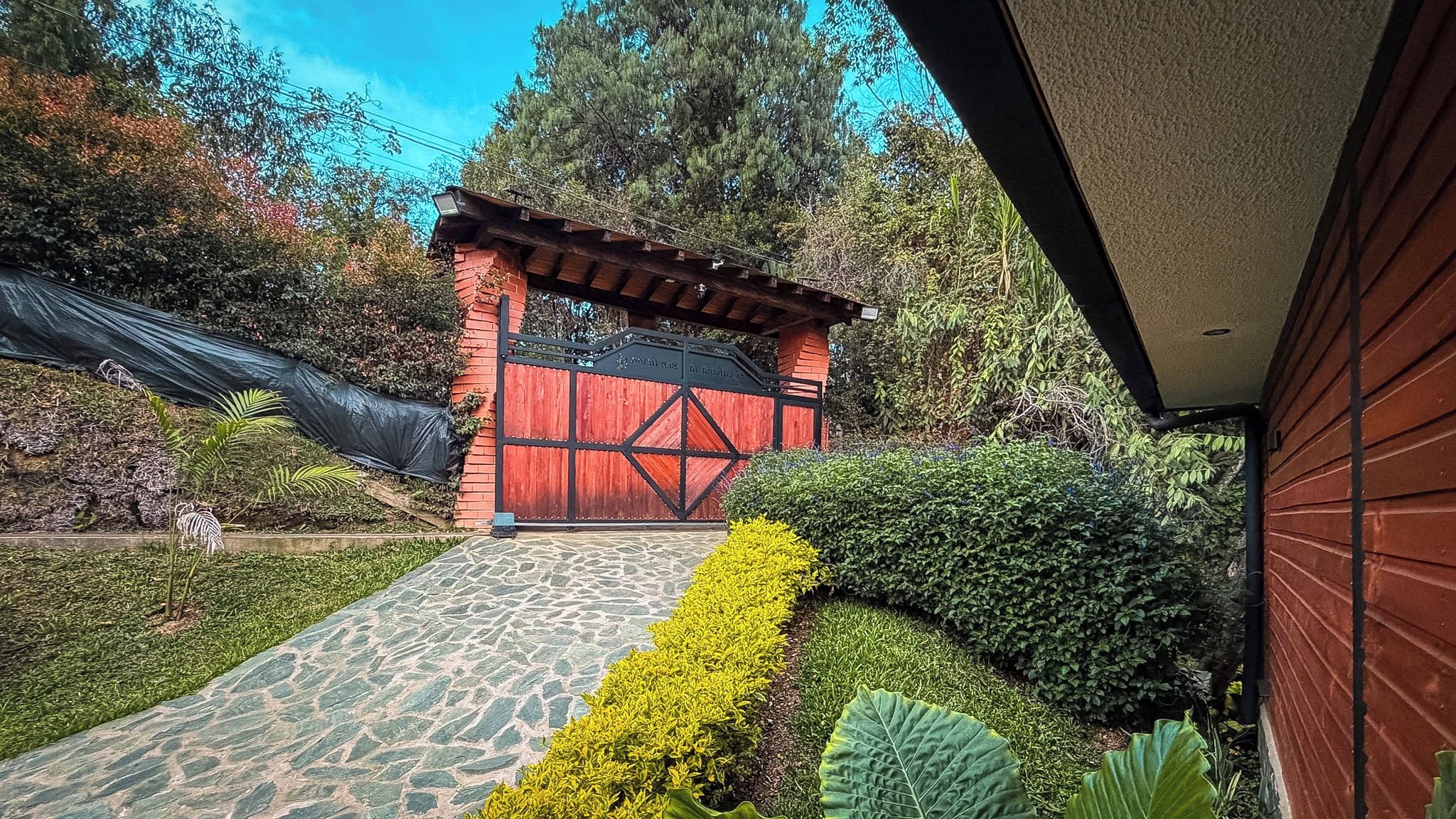A red gate with a wooden roof, a stone pathway, and well-maintained greenery.