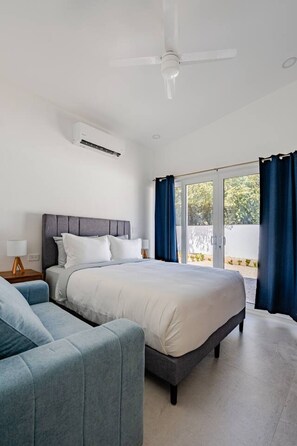 A bedroom with a bed, a nightstand, a lamp, a ceiling fan, and a view through a glass door. - Serene, Contemporary Retreat with Plunge Pool (Playa Avellanas)