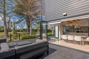 Eine moderne Terrasse im Freien mit Essbereich, einer Sitzecke und einer durch Glastüren einsehbarer Küche.