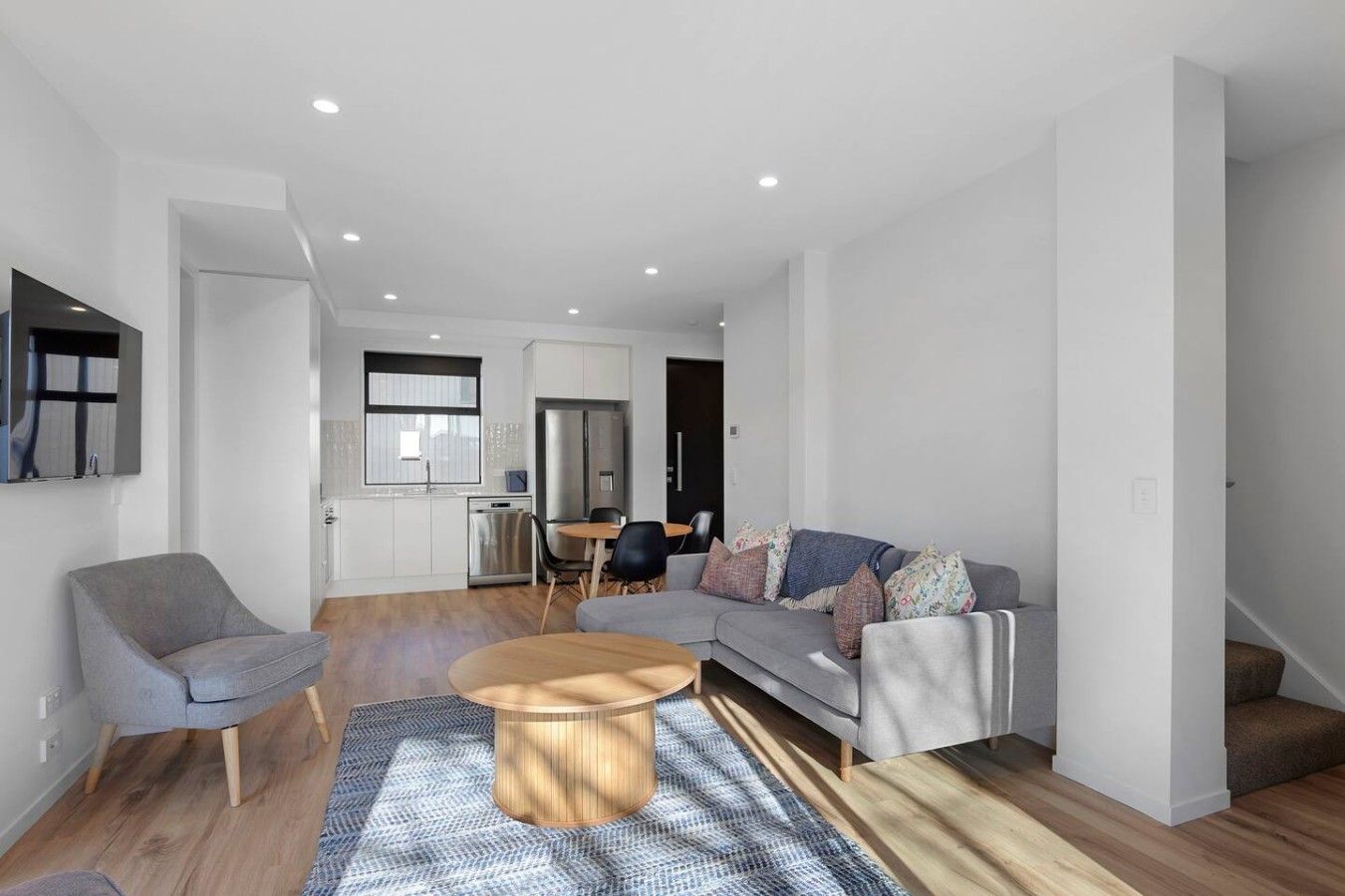 A modern living room with a grey sofa, a round wooden coffee table, and a dining area with a small table and chairs.