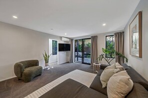 Ein modernes Wohnzimmer mit einer Couch, einem Sessel, einem Flachbildfernseher und einer Glastür, die zu einem Außenbereich führt.