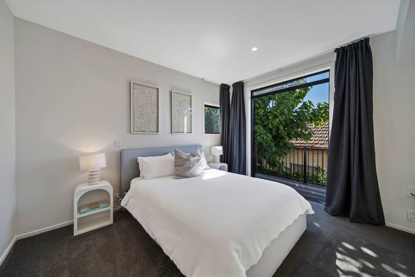 A modern bedroom with a large bed, a bedside table, a nightstand, and a window with curtains. - Modern CBD retreat with parking and courtyard (Christchurch)