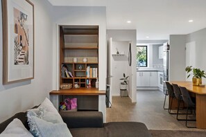 A modern living space with a built-in bookshelf, a dining area with a wooden table and chairs, and a kitchen in the background. - Modern CBD retreat with parking and courtyard (Christchurch)