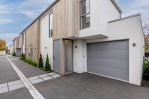 A modern residential building with a grey garage door, a wooden facade, and a paved driveway. - Modern Town House in the Heart of Merivale (Christchurch)