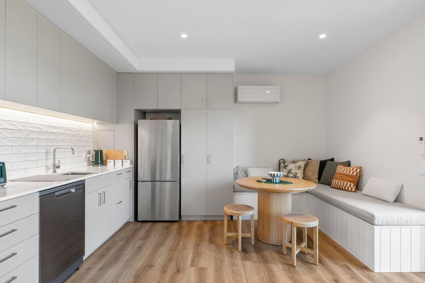 A modern kitchen with a built-in refrigerator, a dining area with stools, and a seating area with cushions.