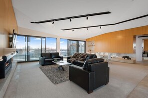 A spacious living area with a fireplace, leather sofas, a coffee table, and a view of the city through large windows. - Luxury Penthouse in the City (Christchurch)