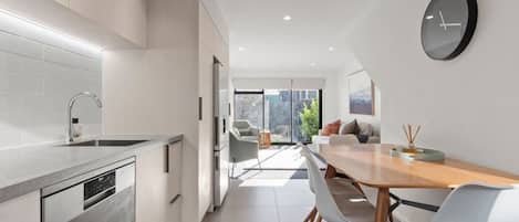 Una cocina moderna con lavavajillas, un comedor con mesa y sillas de madera, y un ventanal que ofrece vistas al exterior.