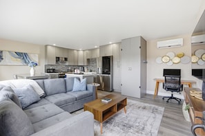 Ein modernes Wohnzimmer mit grauem Sofa, einem Holztisch und einer Küchenzeile mit Edelstahlgeräten.
