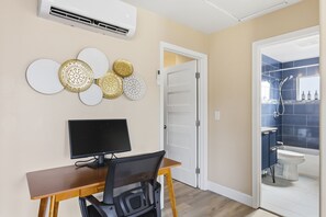 Ein Zimmer mit Schreibtisch, Computer, Wanddekorationen und einem Badezimmer mit Dusche und Toilette.