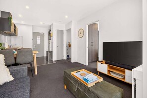 Ein modernes Wohnzimmer mit Flachbildfernseher, einer Couch, einem Couchtisch und einer Essecke mit Tisch und Stühlen.