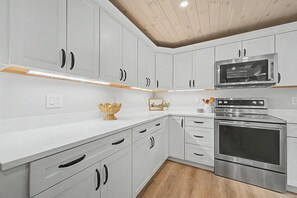 A modern kitchen with white cabinets, a microwave, and a stainless steel oven. - Lake Sunapee Swim & Ski Retreat (Newbury)