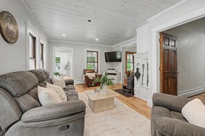 A living room with a fireplace, leather sofas, a coffee table, and a television. - Lake Sunapee Swim & Ski Retreat (Newbury)