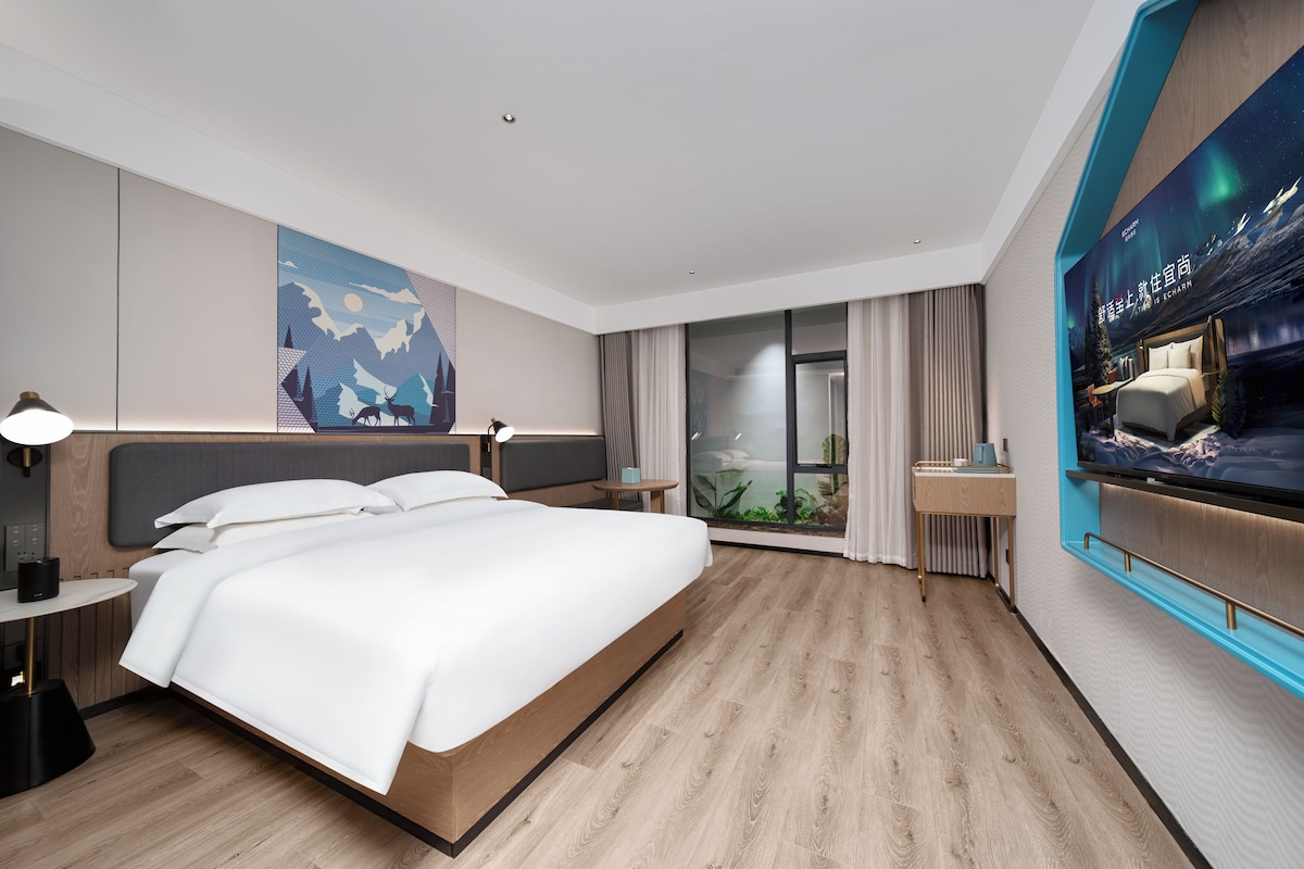 Une chambre d’hôtel moderne avec un grand lit, des tables de chevet, une télévision et une vue sur l’extérieur.
