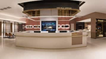 Een moderne hotellobby met een receptiebalie, een groot digitaal scherm en een selfservice kiosk.