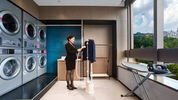 A modern laundry room with multiple Haier washing machines, a drying rack, and a view of a cityscape through large windows.