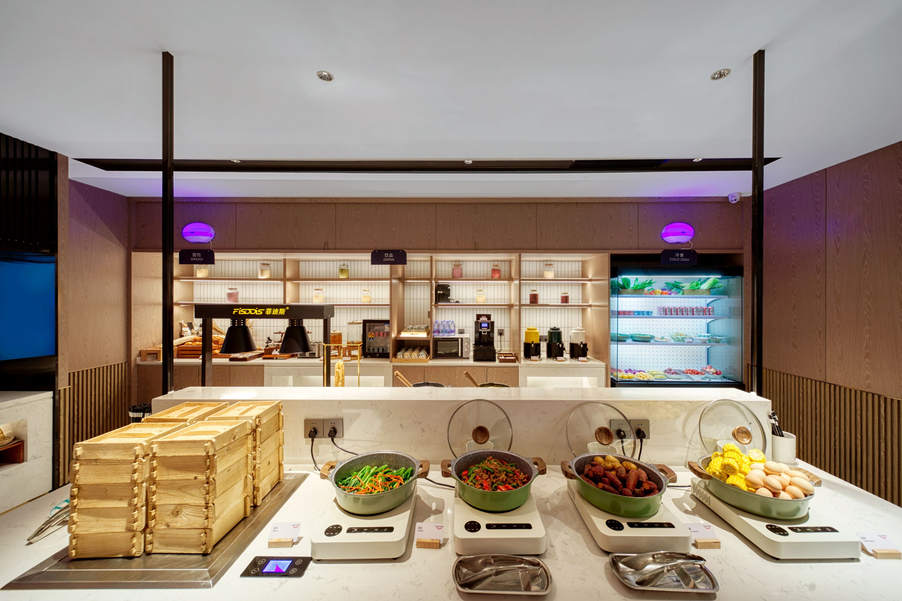 Un espace buffet proposant différents stands de nourriture, notamment un espace réfrigéré et un comptoir où sont présentés les plats.