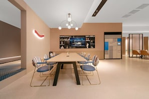 Une salle de conférence d’hôtel équipée d’une longue table, de chaises, d’un téléviseur et d’un espace de casiers en libre-service.