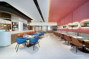 Un café moderne doté d’un bar, de tables et de chaises, et d’un mur orné de motifs.
