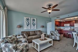 A living room with a sofa, armchairs, a coffee table, and artwork on the wall. A ceiling fan is visible, and there is a kitchen area in the background. - Laketown Perch 1927-Lake Views-Sleeps 8 (Panama City)